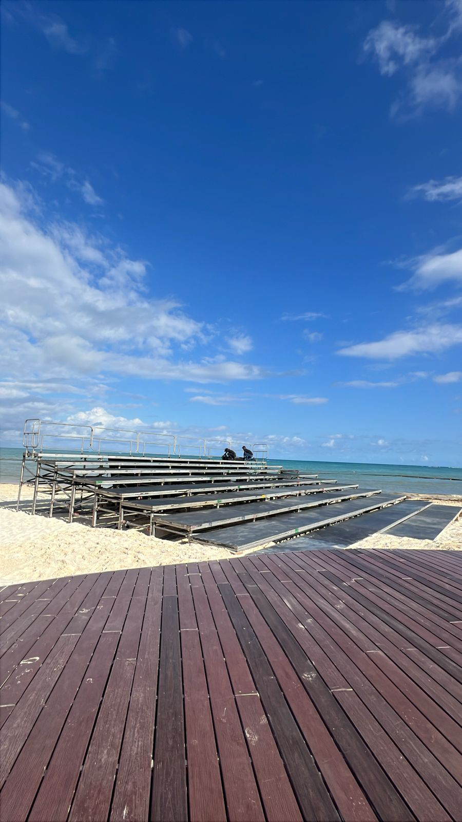 Gradas modulares de andamiaje y madera instaladas en la zona de público de un festival al aire libre, con el escenario principal visible al fondo bajo un cielo despejado